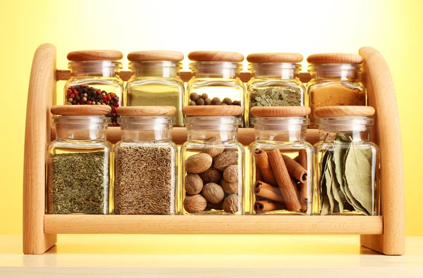 Pulver kryddor i glasburkar på trähylla på gul bakgrund — Stockfoto
