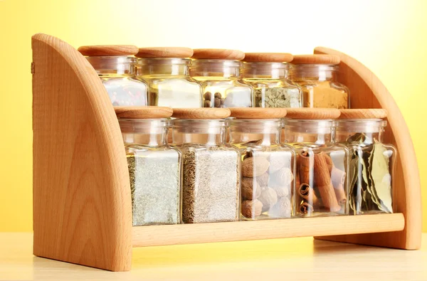 Poeder specerijen in glazen potten op houten plank op gele achtergrond — Stockfoto