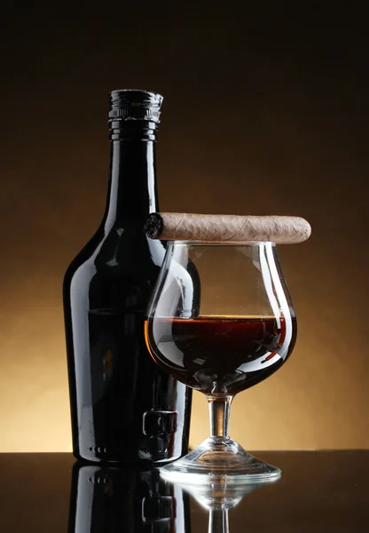 Flaska och glas konjak och cigarrer på brun bakgrund — Stockfoto