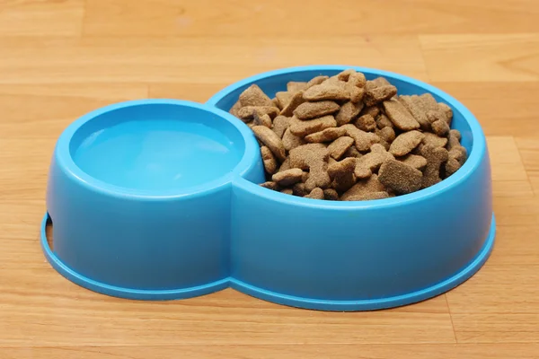Dry dog food and water in blue bowl on the floor — Stock Photo, Image