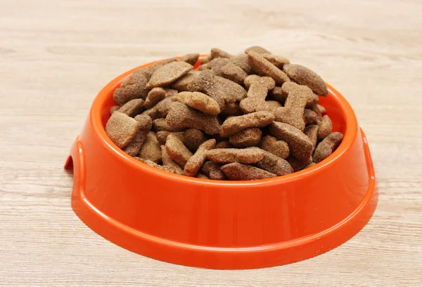 Сухой корм для собак в оранжевой чаше на деревянном фоне — стоковое фото