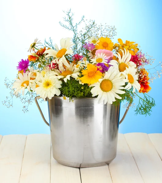 Schöner Strauß heller Wildblumen im Metalleimer, auf Holztisch auf blauem Hintergrund — Stockfoto