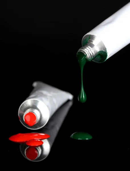 Red and green paints follow from the tubes on black background close-up — Stock Photo, Image