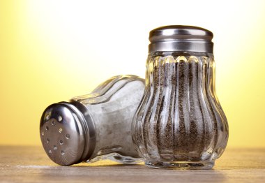 Salt and pepper mills on wooden table on yellow background clipart