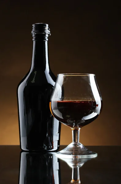 Glas brandy en fles op bruine achtergrond — Stockfoto