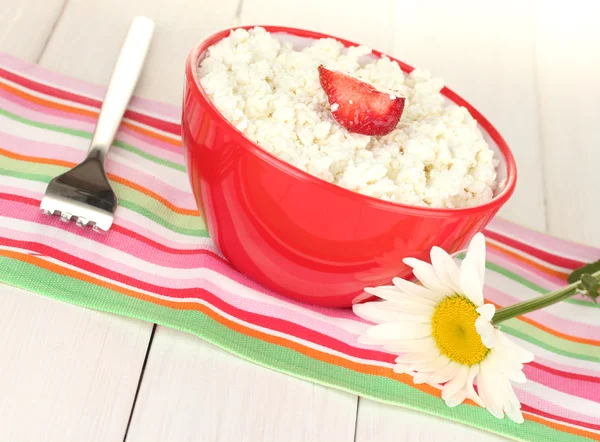 Cottage cheese with strawberry in red bowl, fork and flower on colorful napkin on white wooden table close-up — Stock Photo, Image