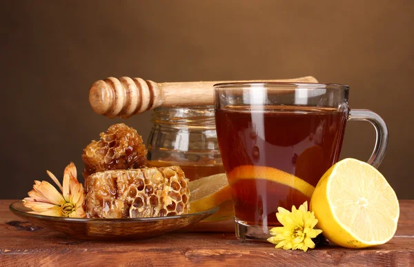 Мед, лимон, соты и чашку чая на деревянном столе на коричневом фоне — стоковое фото