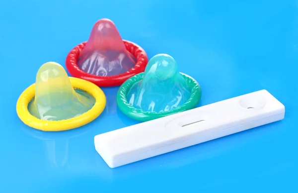 Narození kondomy a těhotenský test na modrém pozadí — Stock fotografie