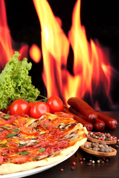 美味披萨、 意大利腊肠、 西红柿和火焰背景上的木桌上的香料 — 图库照片