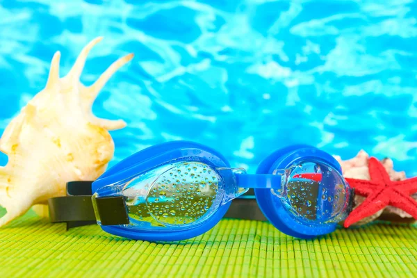 Blauwe zwemmen bril met druppels op een bamboe pad, op blauwe zee achtergrond — Stockfoto