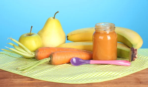Jar with fruit and vegetables baby food, spoon and fruits and vegetables on colorful napkin on blue background — Stock Photo, Image
