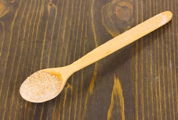 Hnědý cukr v lžíci na dřevěné pozadí — Stock fotografie