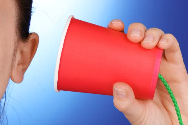 Human ear and paper cup near it close-up on blue background — Stock Photo, Image