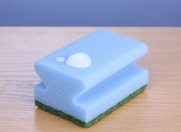 Губка с жидкостью для мытья посуды на деревянном столе на синем фоне — стоковое фото