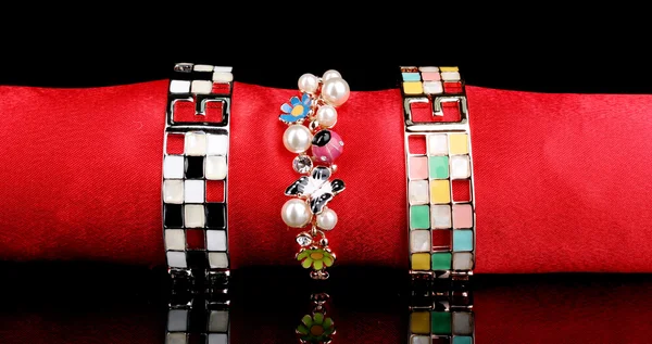 Três belas pulseiras no pano vermelho no fundo preto — Fotografia de Stock