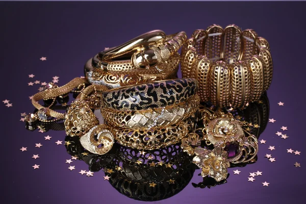 Hermosa joyería dorada sobre fondo púrpura — Foto de Stock