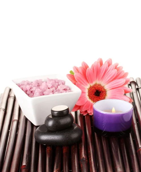Composition of spa stones, bath salt, candle and gerbera on bamboo mat on white background — Stock Photo, Image