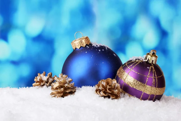 Schöne blaue und lila Weihnachtskugeln und -kegel im Schnee auf blauem Hintergrund — Stockfoto