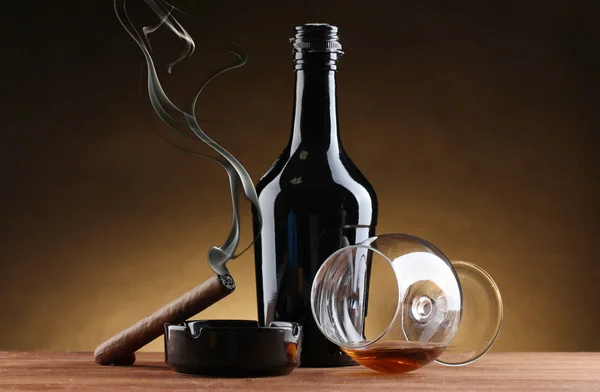Μπουκάλι και ποτήρι κονιάκ και πούρο στο ξύλινο τραπέζι για καφέ φόντο — Φωτογραφία Αρχείου