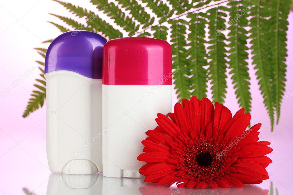 Deodorants with flower and green leaf on pink background