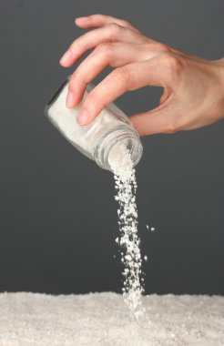 Womans hand holding the salt shaker on grey background close-up clipart