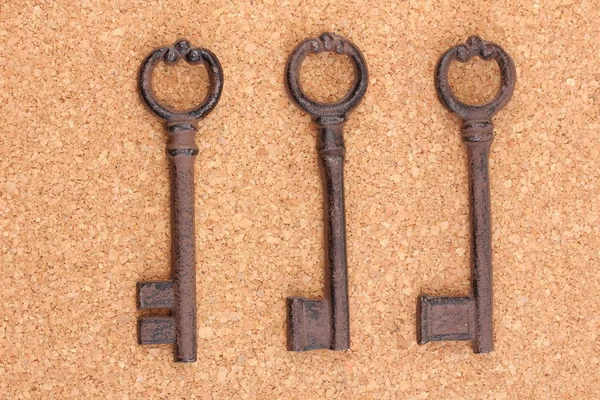 Un montón de llaves antiguas sobre fondo de corcho — Foto de Stock