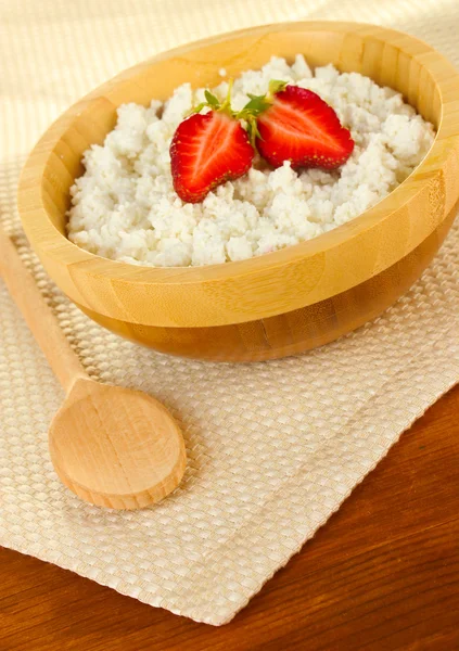 Cottage cheese with strawberry in wooden bowl with wooden spoon on beige napkin on wooden table close-up — Stock Photo, Image