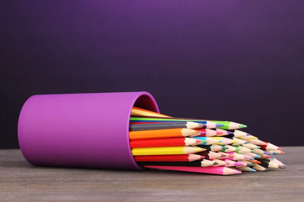 Färgpennor i glas på träbord på violett bakgrund — Stockfoto