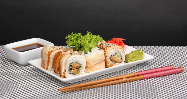 Tasty rolls served on white plate with chopsticks on grey mat on grey background — Stock Photo, Image