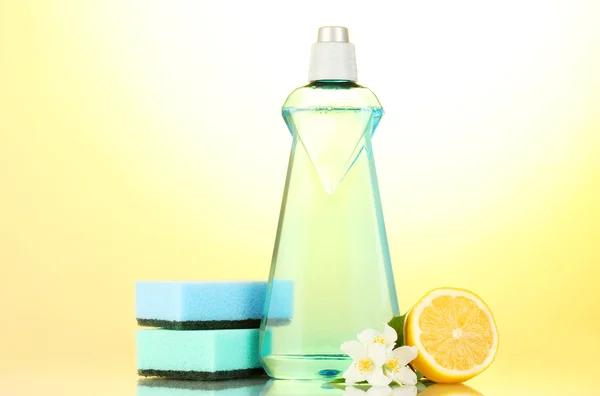 Líquido de lavagem de pratos com esponjas e limão com flores em fundo amarelo — Fotografia de Stock