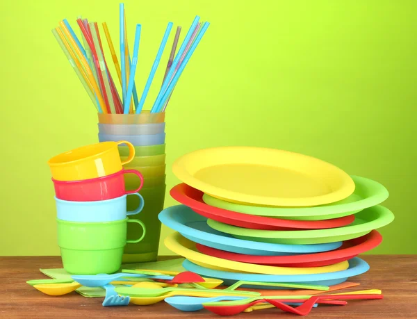 Яскравий пластиковий одноразовий посуд на дерев'яному столі на барвистому фоні — стокове фото