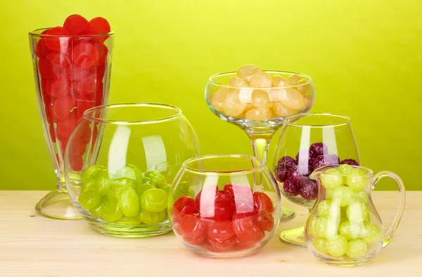 Color candies in glasses on wooden table on green background — Stock Photo, Image