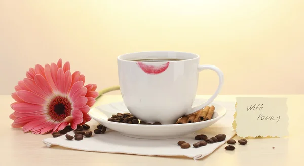 Taza de café con marca de lápiz labial y granos de gerberas, palitos de canela en la mesa de madera — Foto de Stock