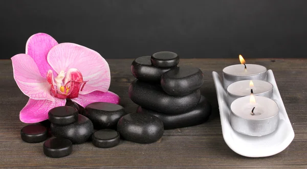 Pedras de spa com flor de orquídea e velas na mesa de madeira no fundo cinza — Fotografia de Stock