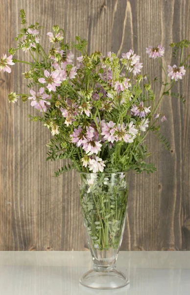 蚕豆上木制背景透明花瓶里的花束 — 图库照片