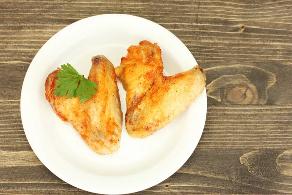 Ali di pollo arrosto con prezzemolo nel piatto su fondo di legno primo piano — Foto Stock