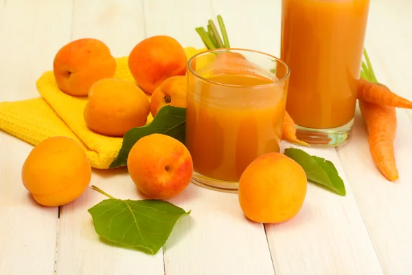 Glasögon med morot och aprikos juice på vita träbord — Stockfoto