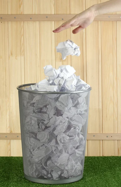 stock image Hand going garbage in metal trash bin from paper on grass on wooden background