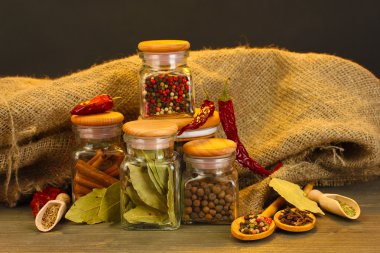 Jars and spoons with spices on wooden table on black background clipart