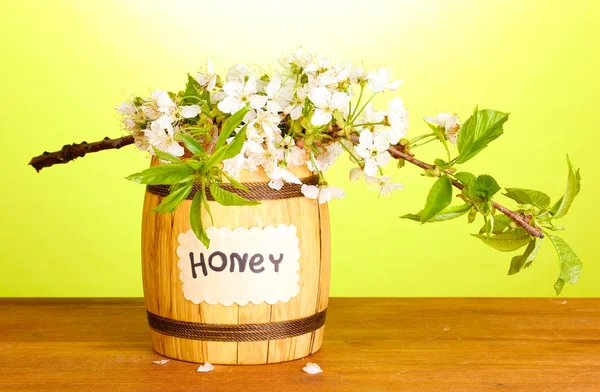 Sweet honey in barrel with blossoming branch on wooden table on green background — Stock Photo, Image