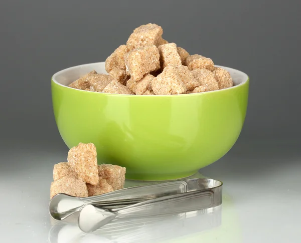 Brunt rörsocker kuber i skålen med socker-tång på grå bakgrund — Stockfoto