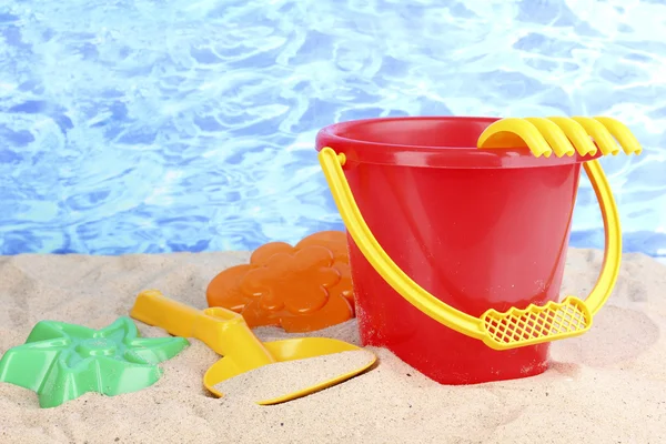 Детские пляжные игрушки на песке на водном фоне — стоковое фото