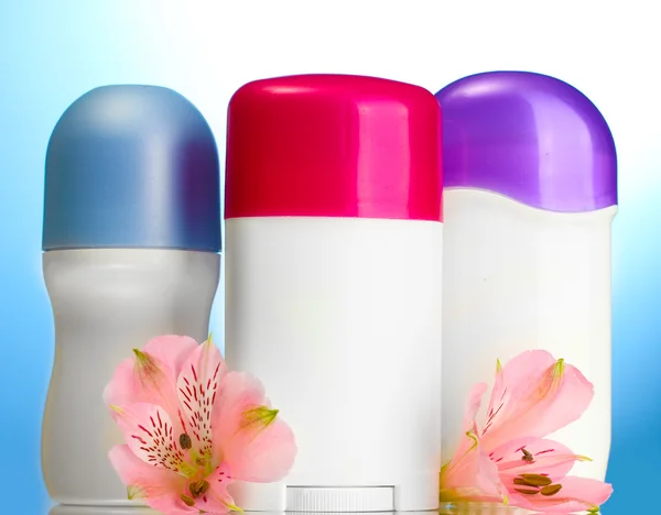 Deodorants with flowers on blue background — Stock Photo, Image