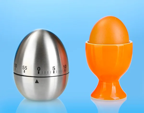 Χρονόμετρο αυγό και το αυγό σε πορτοκαλί σταθεί σε μπλε φόντο — Φωτογραφία Αρχείου