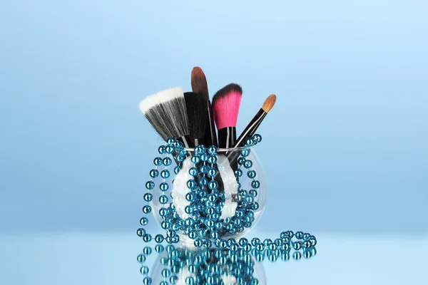 Cepillos de maquillaje en un tazón con collar de perlas sobre fondo azul —  Fotos de Stock