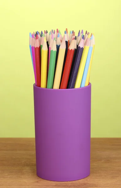 Kleur potloden in glas op houten tafel op groene achtergrond — Stockfoto
