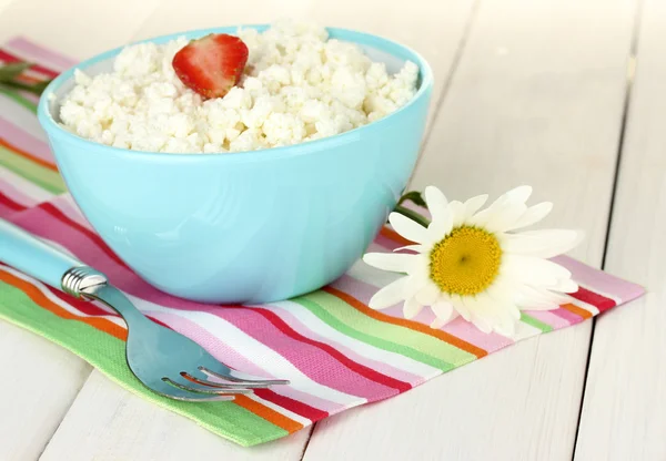 Cottage fromage à la fraise dans un bol bleu, fourchette et fleur sur serviette colorée sur table en bois blanc close-up — Photo