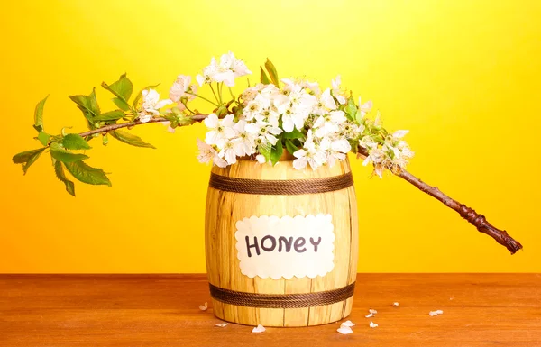 Sweet honey in barrel with blossoming branch on wooden table on yellow background — Stock Photo, Image