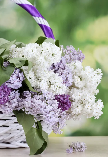 Beautiful lilac flowers in basket on wooden table on green background — Stock Photo, Image
