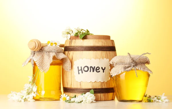 Сладкий мед в бочке и банки с цветами акации на деревянном столе на желтом фоне — стоковое фото